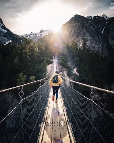 A traveller crossing a rope bridge between mountains