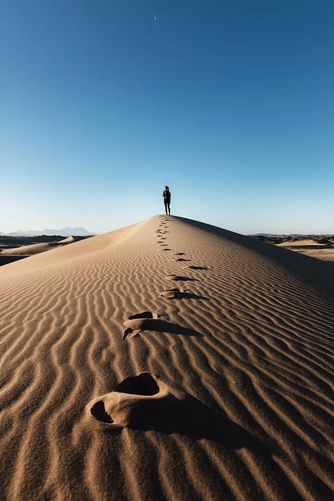 Footprints climbing a desert dune under a blue sky